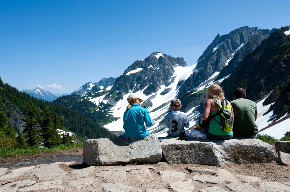 Family resting together at Cascade Pass with Pelton Basin beyond